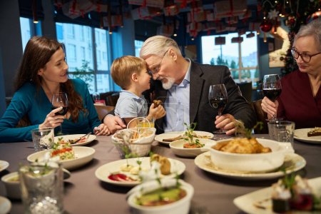 Photo for Playful aged man with little boy enjoying festive time spending together while having Christmas dinner in restaurant - Royalty Free Image