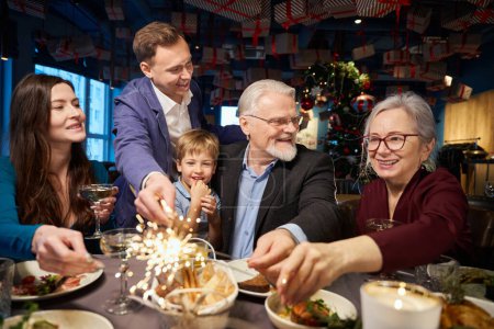 Téléchargez les photos : Joyeuse famille célébrant le Nouvel An au restaurant avec étincelant profiter de la nuit festive ensemble - en image libre de droit