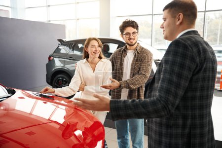 Photo for Man and woman choosing and buying car at car showroom salesman helps them to make right decision - Royalty Free Image