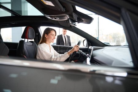 Téléchargez les photos : Femme satisfaite d'essayer une nouvelle voiture en choisissant la voiture avec l'aide du vendeur dans le concessionnaire - en image libre de droit