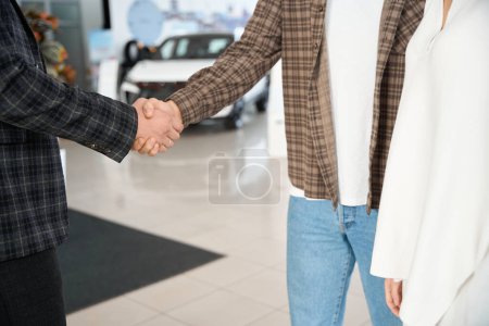 Téléchargez les photos : Homme méconnaissable serrant la main avec le vendeur après avoir acheté une automobile au centre de concession - en image libre de droit