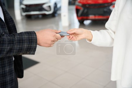 Photo for Unrecognizable man dealer giving car key to woman in automotive dealership showroom - Royalty Free Image