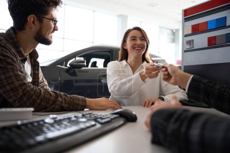 Photo for Happy woman taking keys of new car couple buying automobile sitting in office with manager in dealership - Royalty Free Image