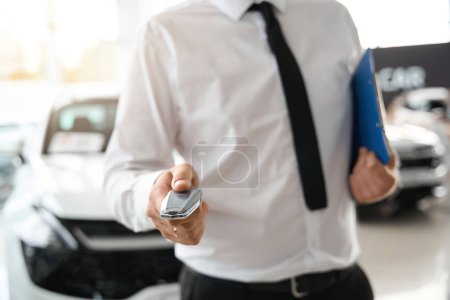 Téléchargez les photos : Homme méconnaissable tenant des clés d'automobile dans le concessionnaire automobile après avoir signé des documents d'achat de voiture - en image libre de droit