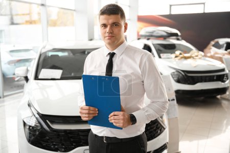 Photo for Successful male shop assistant holding clipboard at automobile car dealer shop - Royalty Free Image