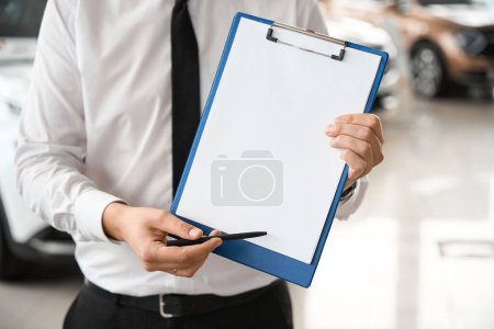 Photo for Unrecognizable anonymous male shop assistant holding clipboard at automobile car dealer shop - Royalty Free Image