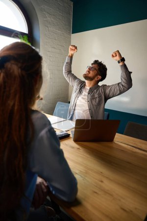 Photo for Cropped businesswoman looking at young excited successful caucasian male colleague celebrating win in work at desk in coworking office. Concept of modern business lifestyle - Royalty Free Image