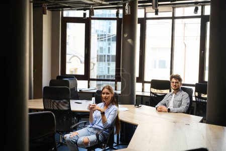 Téléchargez les photos : Jeune homme d'affaires caucasien souriant et femme d'affaires buvant du thé ou du café regardant la caméra pendant le travail dans un bureau de coworking. Concept de pause et de repos au travail - en image libre de droit