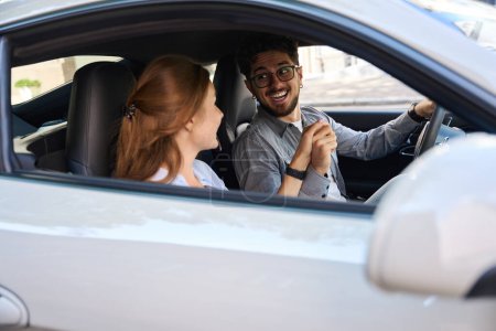 Téléchargez les photos : Jeune homme caucasien excité et femme souriante tenant la main et se regardant dans l'automobile. Concept de relation amoureuse. Idée de voyage, de voyage et de vacances - en image libre de droit