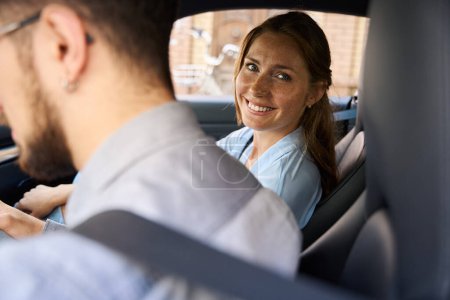 Photo for Young caucasian woman looking at camera from car while riding with her cropped boyfriend on foreground. Concept of road trip, travelling and vacation - Royalty Free Image