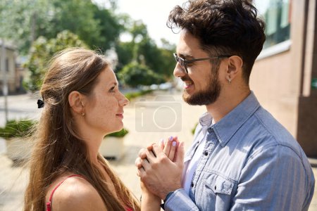 Photo for Cropped side view of young happy caucasian couple holding hands and looking at each other in city at warm summer day. Concept of romantic relationship, closeness and date - Royalty Free Image