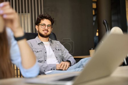 Foto de Selective focus of smiling caucasian male employee with smartphone looking at partial female colleague in coworking office. Concept of break and rest at work - Imagen libre de derechos