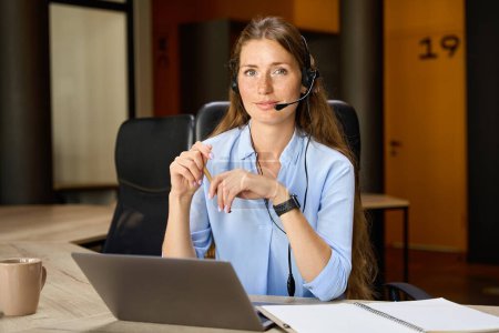 Foto de Young serious female caucasian call center operator looking at camera during work at desk in coworking office. Concept of modern business lifestyle - Imagen libre de derechos