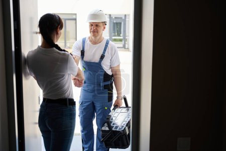 Téléchargez les photos : Woman and adult caucasian male worker handshaking in entrance to new modern townhouse before repair in warm sunny day. Concept of work deal - en image libre de droit
