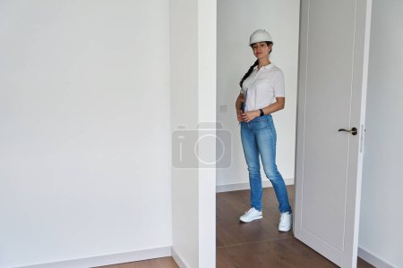 Foto de Serious adult caucasian female designer holding clipboard and looking at camera in new empty modern comfortable townhouse - Imagen libre de derechos
