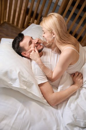 Photo for Young spouses are having fun on a comfortable bed, the couple is staying in a honeymoon suite - Royalty Free Image