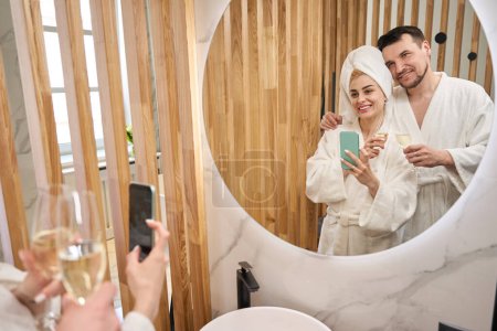 Téléchargez les photos : Happy newlyweds taking a selfie in the bathroom, woman wearing a towel turban - en image libre de droit