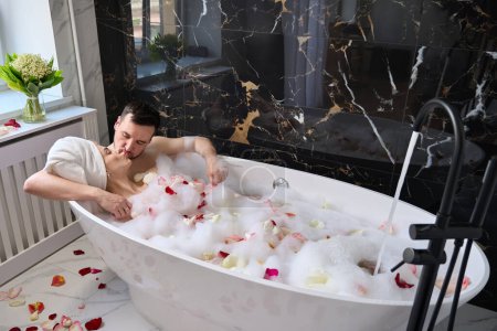 Foto de Newlyweds kiss in a foam bath with rose petals, a man tenderly hugs his wife - Imagen libre de derechos
