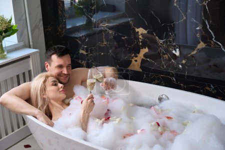 Téléchargez les photos : Happy couple enjoying champagne in a foam bath, man tenderly hugging woman - en image libre de droit