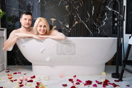 Téléchargez les photos : Newlyweds soak in the bathtub, the floor is decorated with rose petals - en image libre de droit