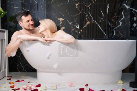 Téléchargez les photos : Happy newlyweds enjoying a warm bath, the floor is decorated with rose petals - en image libre de droit