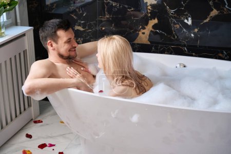 Téléchargez les photos : Man and woman enjoying warm bubble bath, floor decorated with rose petals - en image libre de droit