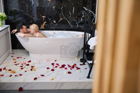 Téléchargez les photos : Young couple enjoying a warm bubble bath, the floor is decorated with rose petals - en image libre de droit