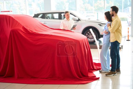 Photo for People are standing by the car under a red cover, the husband has prepared a surprise for his wife - Royalty Free Image