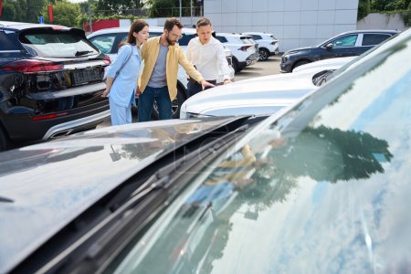 Photo for Buyers with a consultant inspect cars in the courtyard of a car dealership, a man examines a popular model - Royalty Free Image