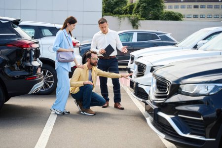 Photo for Car dealership employee advises spouses when choosing a car, a man examines a popular model - Royalty Free Image