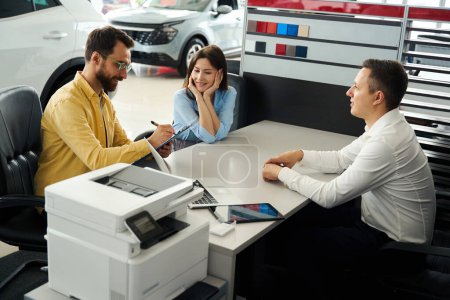 Photo for Buyers finalize a deal in the office area of a car dealership, a man signs documents - Royalty Free Image