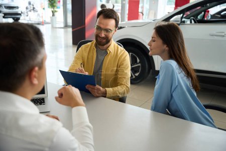 Téléchargez les photos : People make a deal in the office area of a car dealership, a man signs documents - en image libre de droit