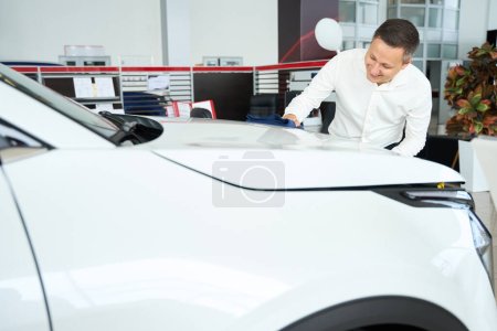 Foto de Manager wipes the hood of a car with a soft napkin, he works in a car dealership - Imagen libre de derechos