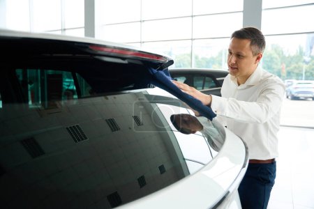 Téléchargez les photos : Male wipes the car glass with a soft napkin, he works in a car dealership - en image libre de droit
