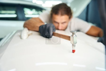 Téléchargez les photos : Guy smoothes out dents on the door of a white car, he uses a special straightening hammer - en image libre de droit