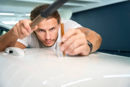 Téléchargez les photos : Auto repairman uses a straightening stick to level out body dents - en image libre de droit