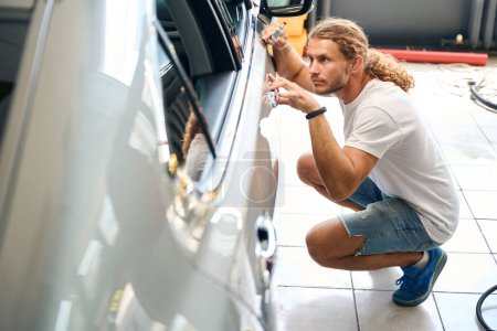 Photo for Long-haired man smooths out dents on a car door with a straightening hammer, he works in a car repair shop - Royalty Free Image