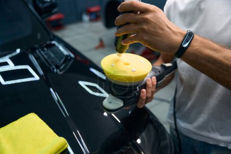Foto de Detailing a black car in a car repair shop, the master applies special wax to the grinder - Imagen libre de derechos