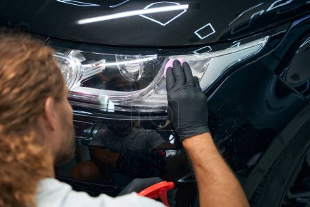 Foto de Male is working in a car workshop detailing a black car, he is using protective gloves - Imagen libre de derechos