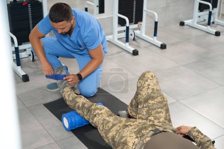 Téléchargez les photos : Male rehabilitator works with a military patient in the gym, he restores the functionality of the patients leg muscles - en image libre de droit