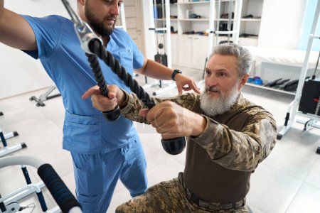 Téléchargez les photos : Doctor rehabilitation specialist works with a patient in the gym, a man sits on a fitball - en image libre de droit