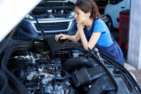 Photo for Specialist car mechanic uses a laptop for work, she is located under the open hood of a car - Royalty Free Image