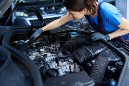 Téléchargez les photos : Jeune mécanicienne répare une voiture, elle utilise un outil spécial - en image libre de droit