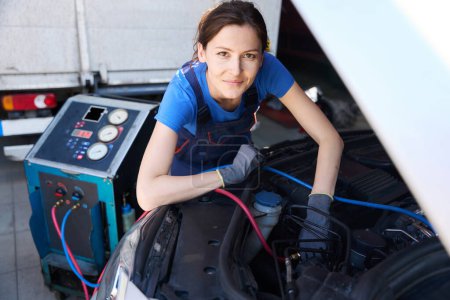 Téléchargez les photos : Spécialiste mécanicien automobile en salopette remplit un climatiseur de voiture, une femme utilise un équipement spécial - en image libre de droit