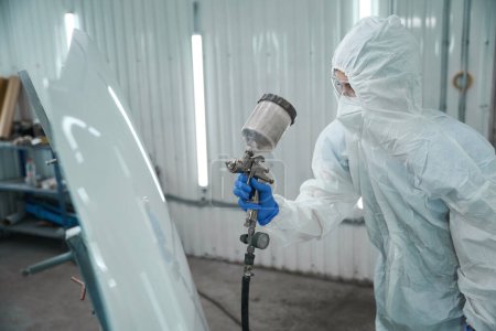 Photo for Specialist uses a paint injection tank at work, she is wearing protective overalls, goggles and a respirator - Royalty Free Image