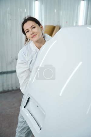 Foto de Mujer linda en equipo protector blanco en una tienda de pintura, ella tiene una pieza de coche blanco - Imagen libre de derechos
