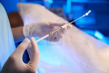 Nahaufnahme von Arzthänden mit einer Spritze zur künstlichen Befruchtung in einer unscharfen Reproduktionsklinik. Embryologie und Biotechnologie