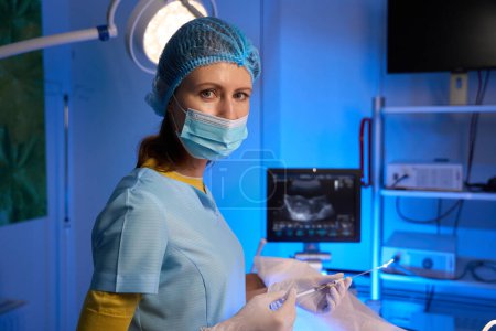 Téléchargez les photos : Vue latérale partielle du médecin féminin utilisant une seringue pour le transfert d'embryons et regardant la caméra dans une clinique de reproduction. Embryologie et biotechnologie - en image libre de droit