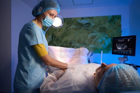 Foto de Doctora examinando a una paciente en equipo de ultrasonido y mirándola en clínica reproductiva. Concepto de embarazo y maternidad - Imagen libre de derechos