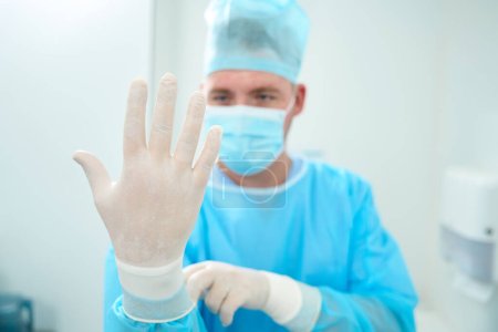 Photo for Cropped image of blurred male caucasian doctor put on latex glove on hand before surgery in clinic. Healthcare and hygiene - Royalty Free Image
